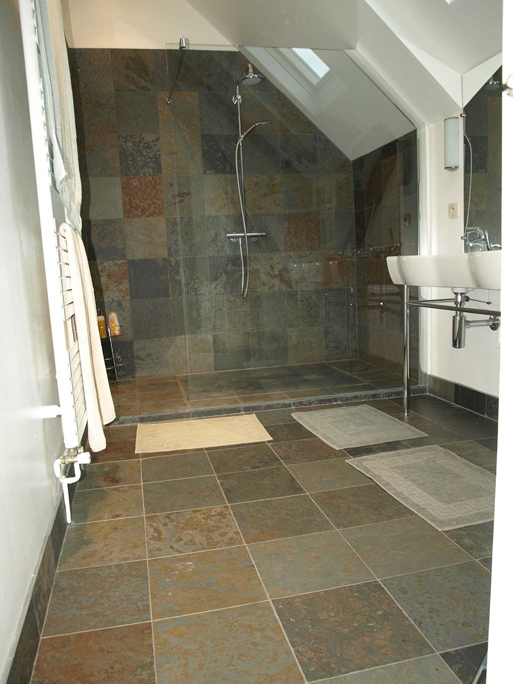 Une salle de bains moderne avec sol en ardoise et douche à l'italienne, dotée d'un plafond mansardé et d'un meuble-lavabo à double vasque.