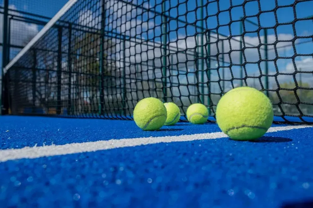 Hay tres pelotas de tenis en una cancha de tenis al lado de una red.