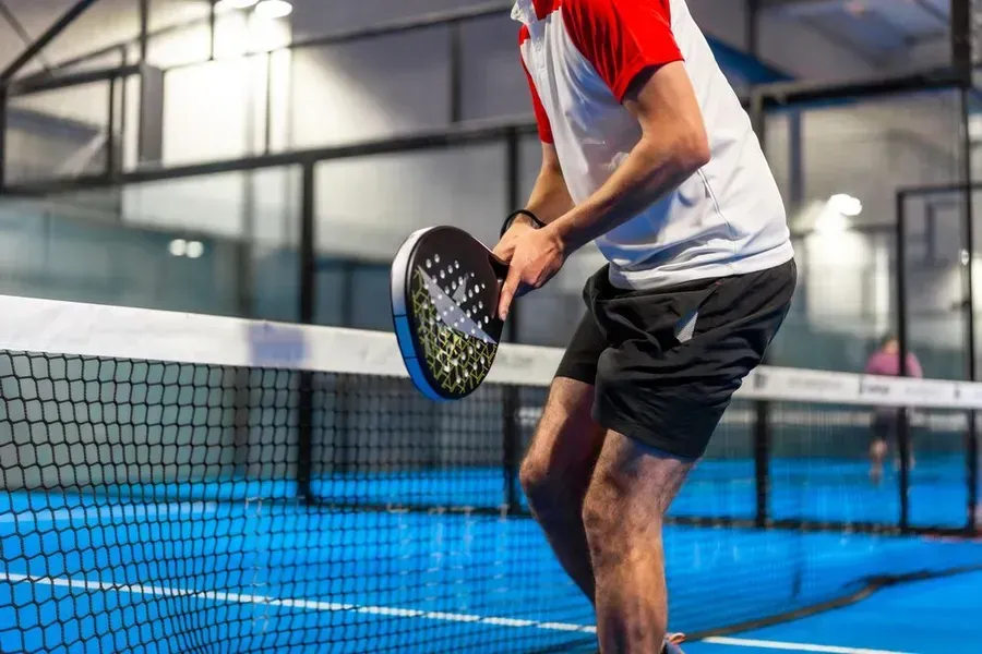 Un hombre está jugando al pádel en una cancha azul.