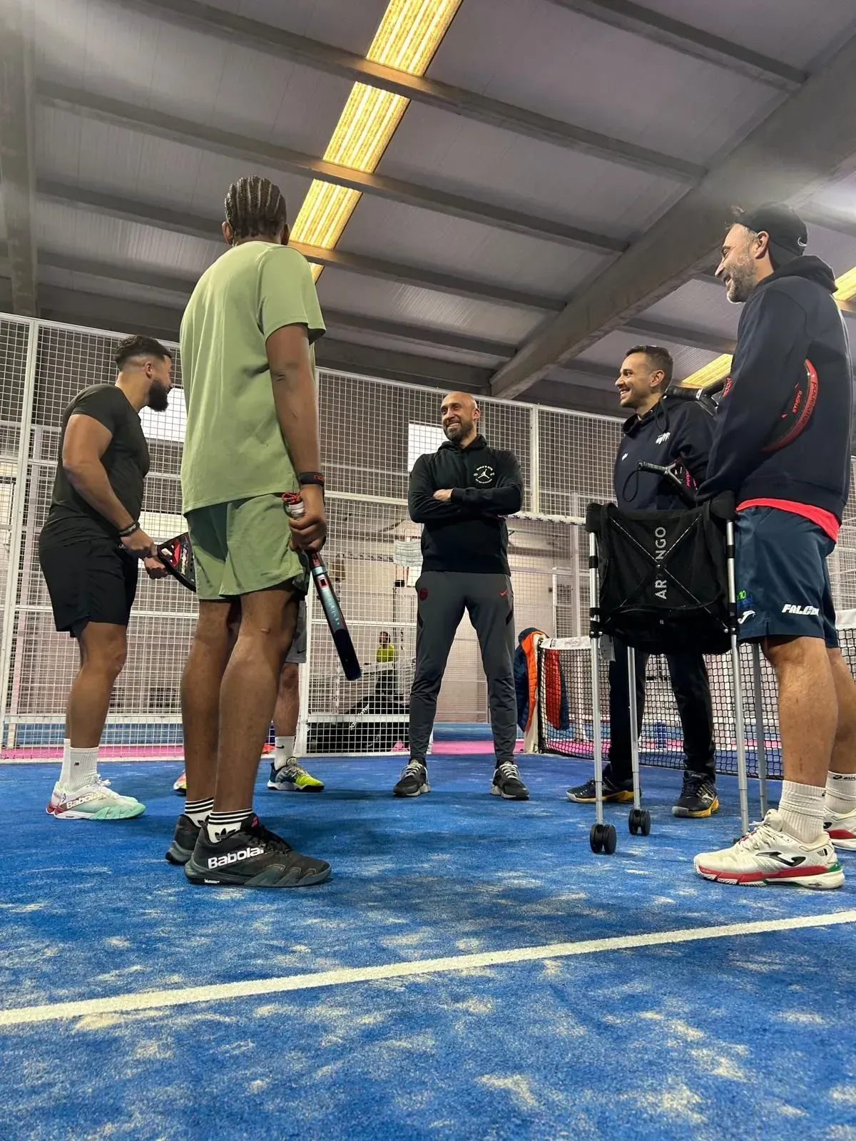 Un grupo de hombres están de pie en una cancha de tenis hablando entre ellos.