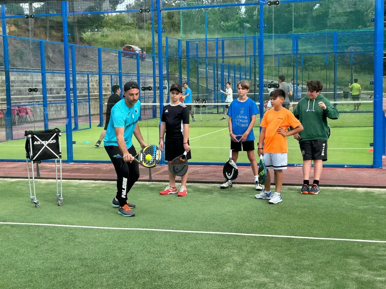 Un hombre está enseñando a un grupo de niños pequeños a jugar al pádel.