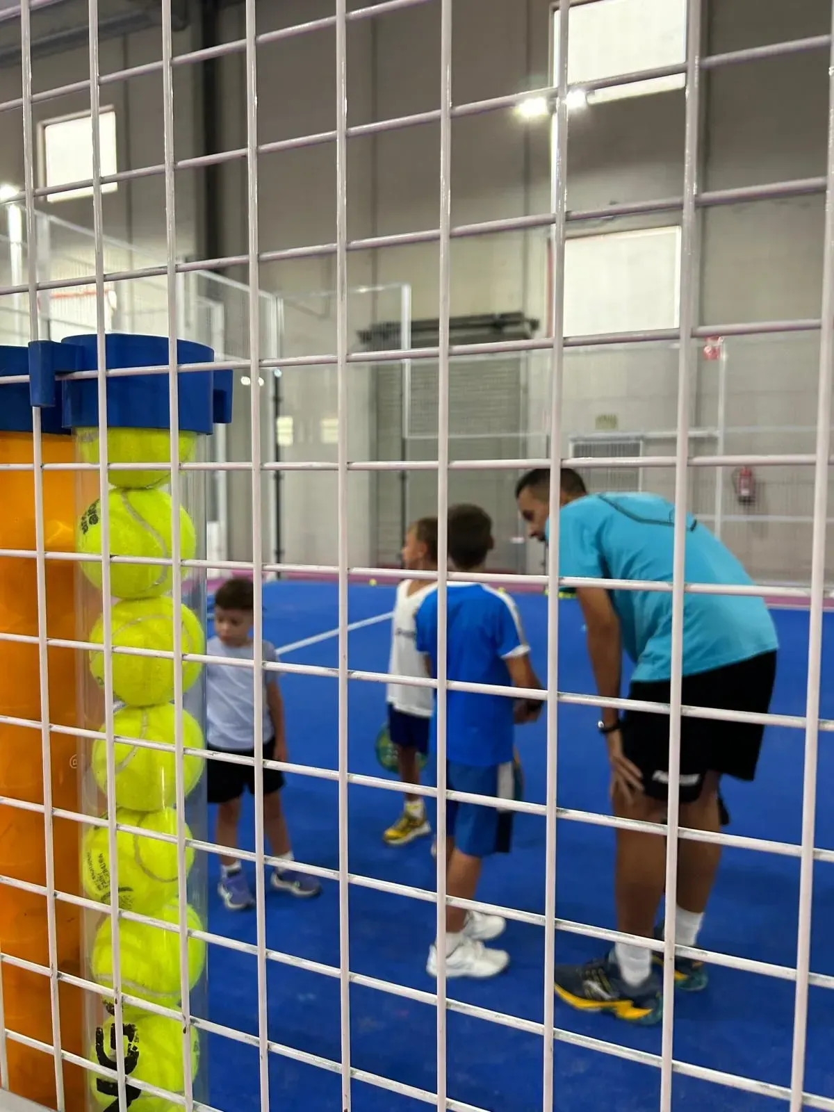 Un hombre con una camisa azul se encuentra frente a un montón de pelotas de tenis.