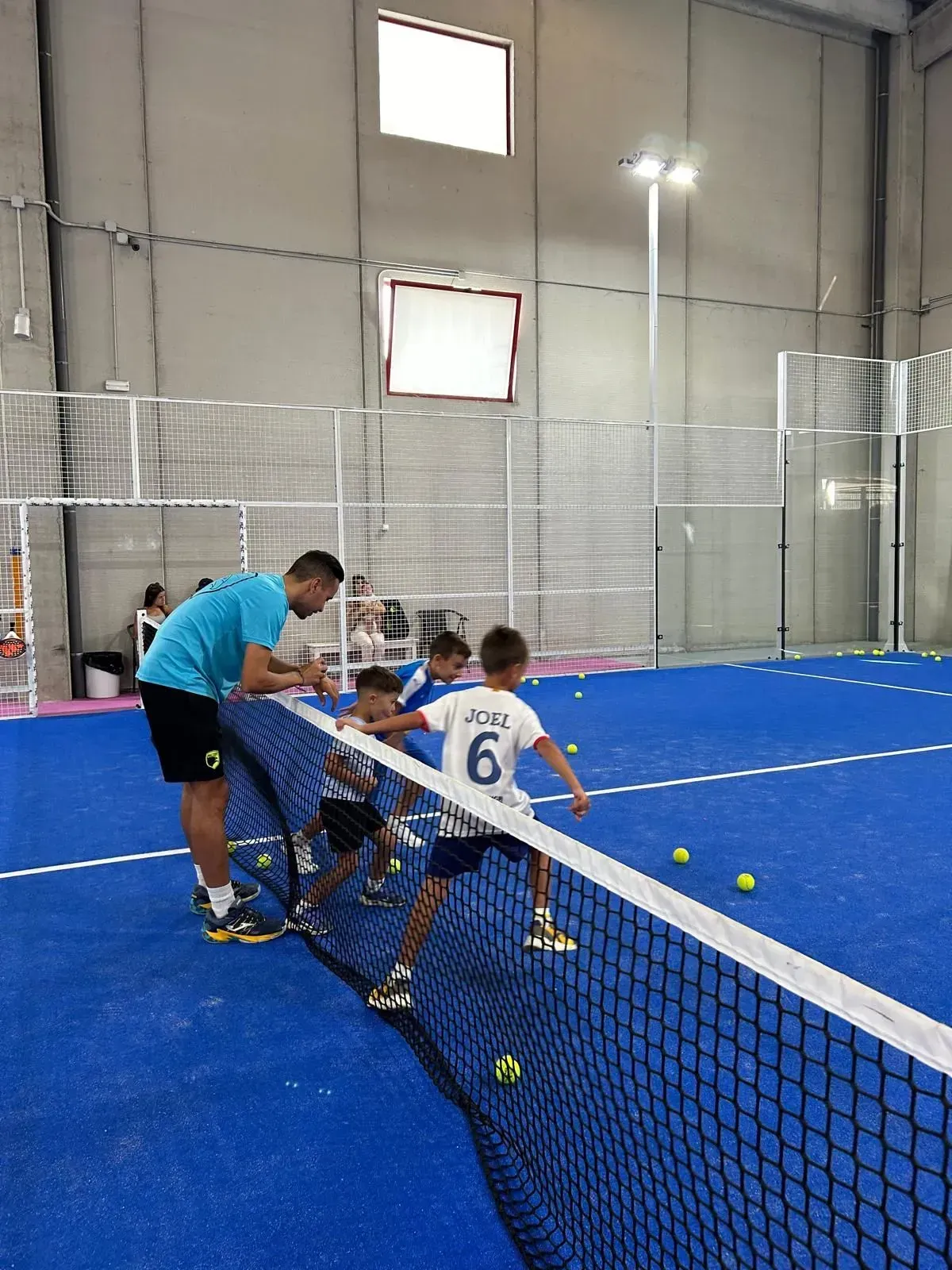 Un grupo de chicos jóvenes están jugando al tenis en una cancha.
