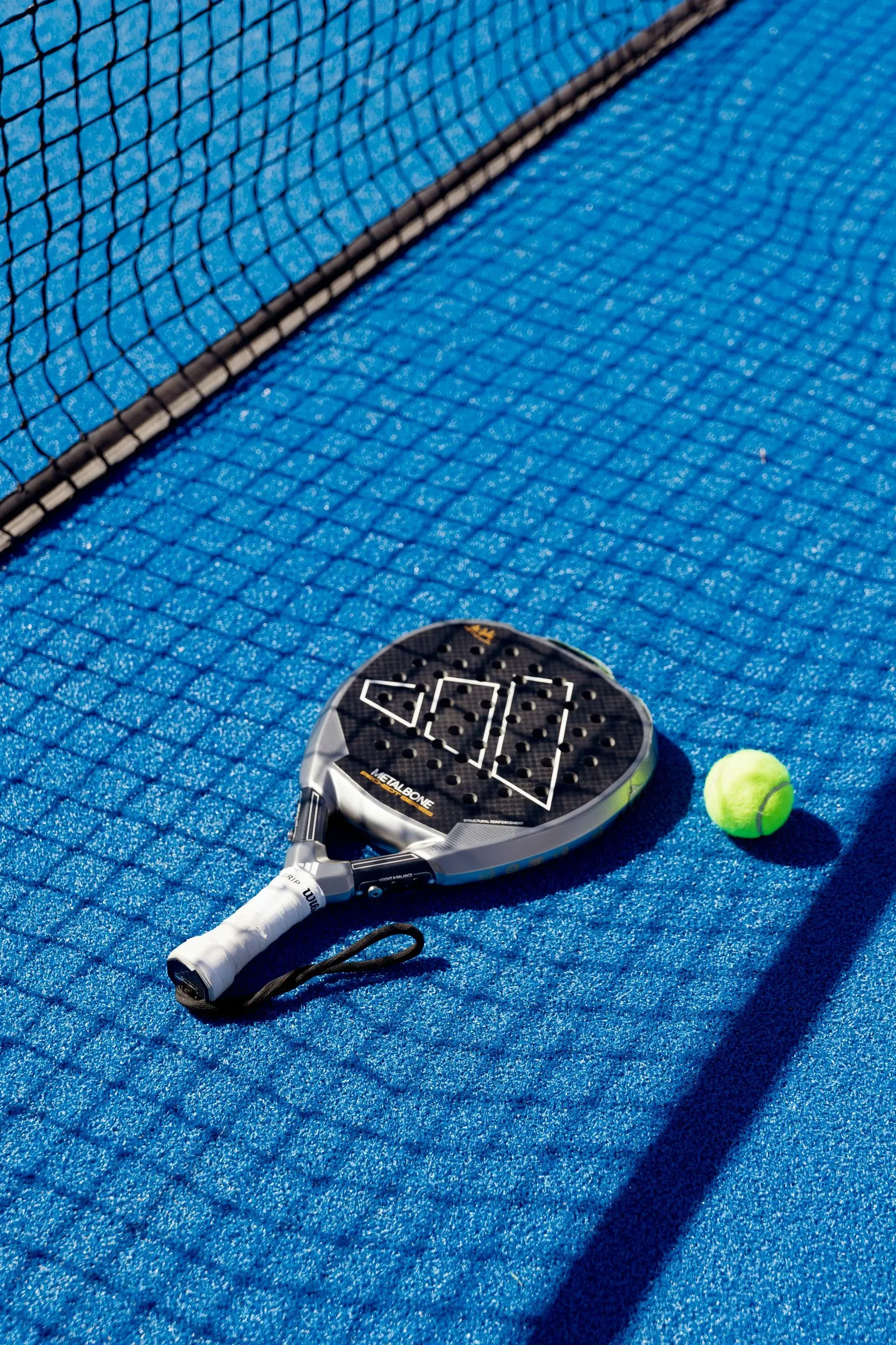 Una raqueta y una pelota de pádel están en una cancha de tenis azul.
