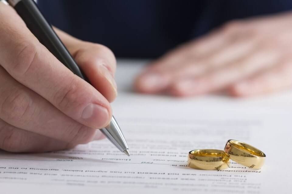 Una persona está escribiendo en un trozo de papel al lado de un par de anillos de boda.