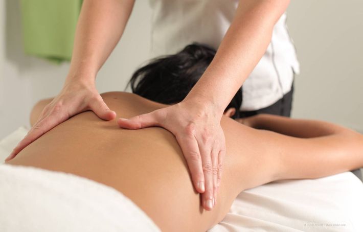 Frau, die eine Rückenmassage erhält und mit dem Gesicht nach unten auf einem Massagetisch liegt.