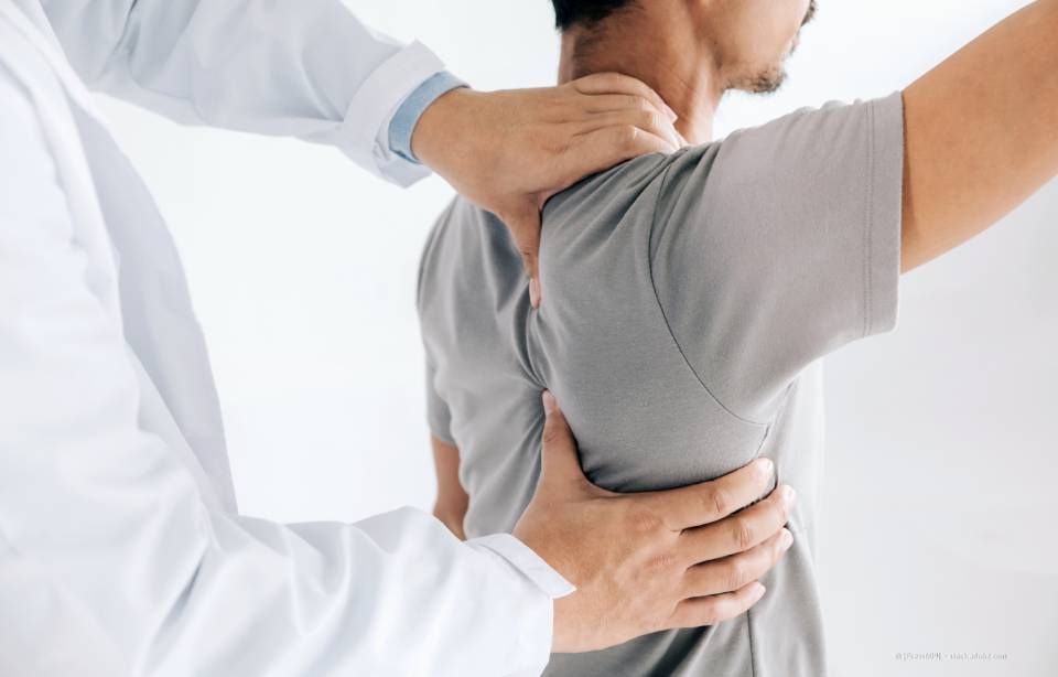 Ein Arzt untersucht in einer Klinik den Rücken und Nacken eines Patienten, wahrscheinlich um nach Schmerzen oder Verletzungen zu suchen.