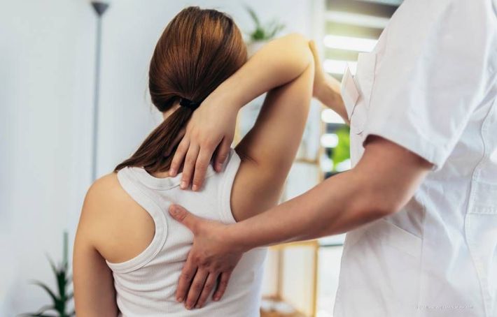 Frau erhält chiropraktische Behandlung. Die Hände des Chiropraktikers liegen auf ihrem Rücken und strecken ihren Arm. Drinnen, natürliches Licht.