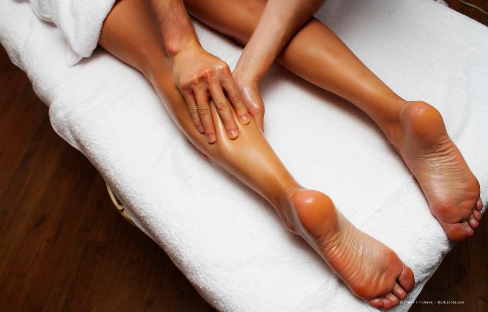 Die Hände eines Masseurs massieren das eingeölte Bein einer Person auf einem weißen Handtuch.