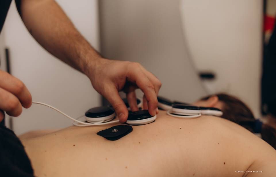 Der Rücken einer Person mit Elektrotherapie-Pads, während ein Therapeut die Pads anpasst.