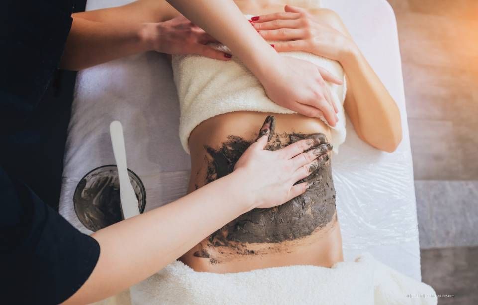 Person, die in einem Spa eine Schlammpackung erhält; Hände tragen Schlamm auf den Bauch auf.