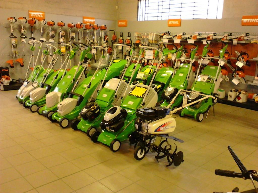 Tondeuses à gazon et motoculteurs exposés dans un magasin ; verts et blancs, avec d'autres outils visibles sur les étagères.