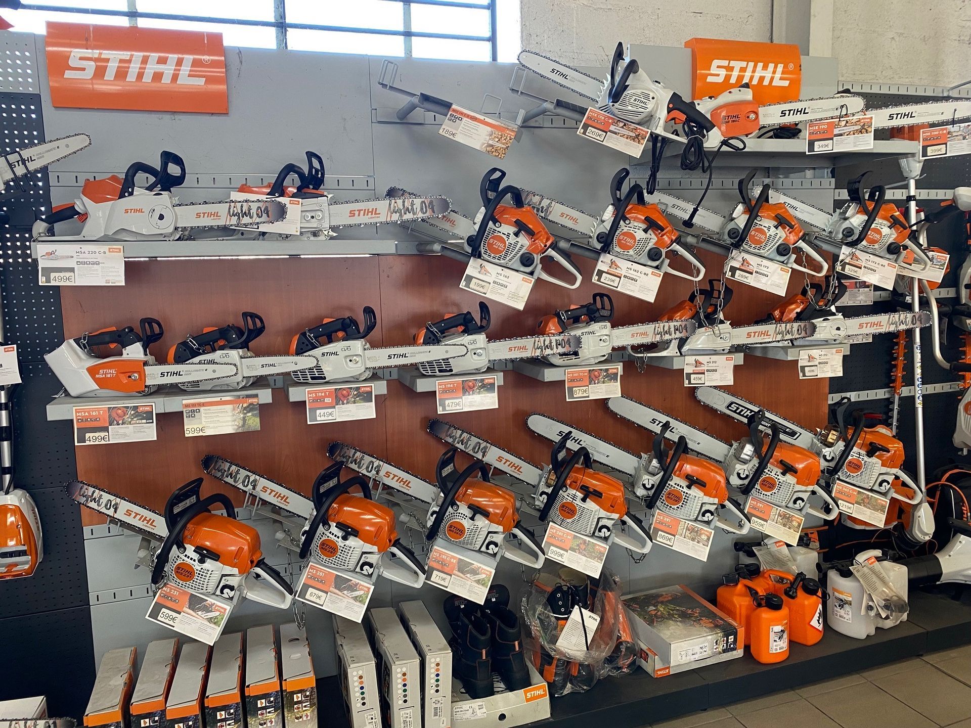 Tronçonneuses exposées sur des étagères dans un magasin, plusieurs avec des détails orange et blancs et le logo « STIHL ».