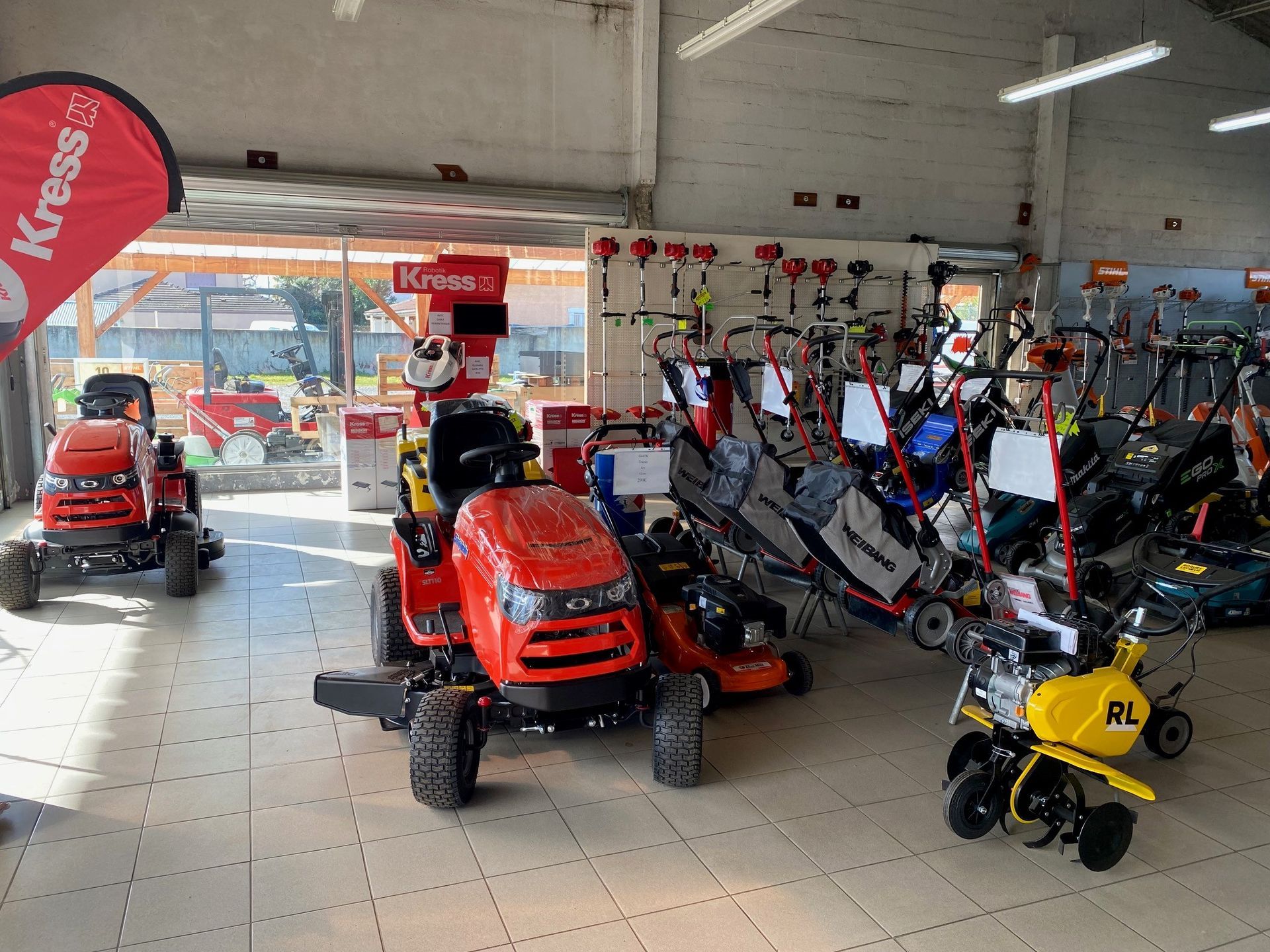 À l'intérieur d'un magasin : tracteurs à gazon, tondeuses et équipements de jardinage exposés sous des lumières vives.