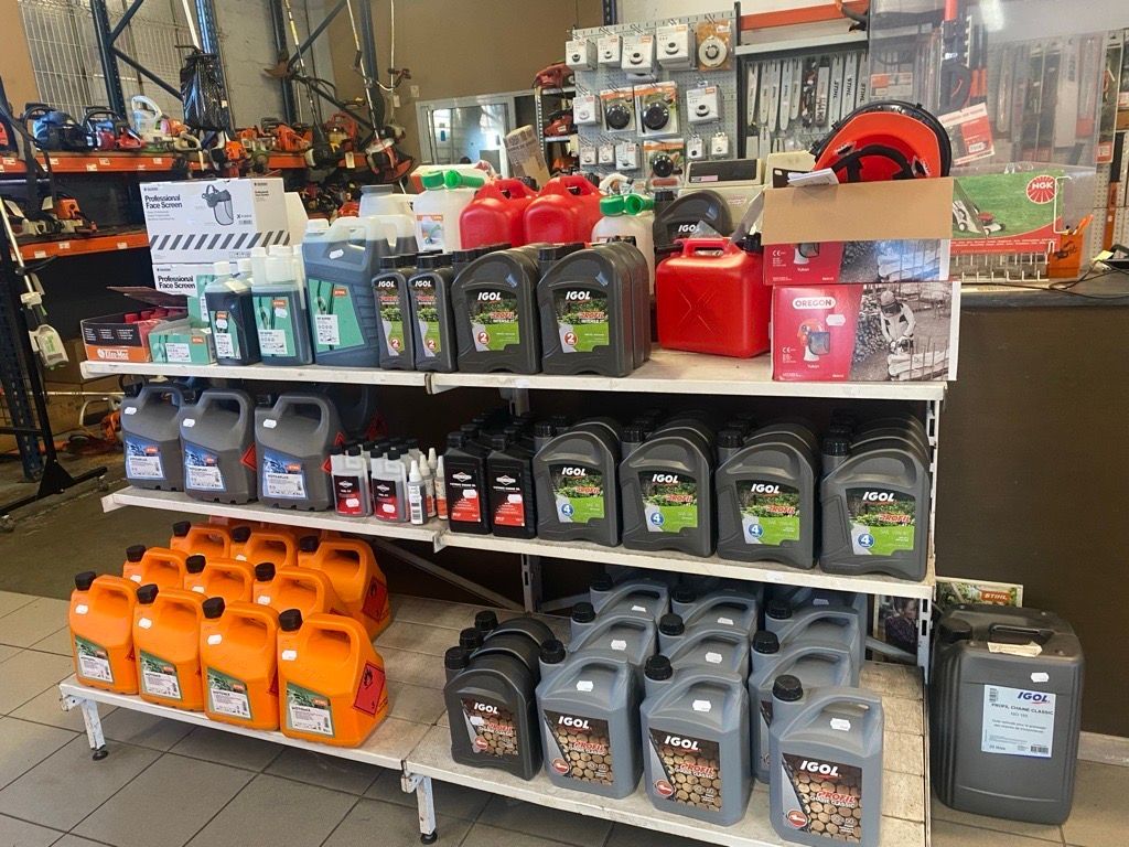 Bidon d'essence rouge sur béton avec voiture en arrière-plan.