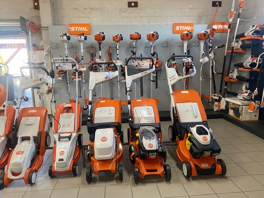 Tondeuses à gazon et motoculteurs exposés dans un magasin ; verts et blancs, avec d'autres outils visibles sur les étagères.