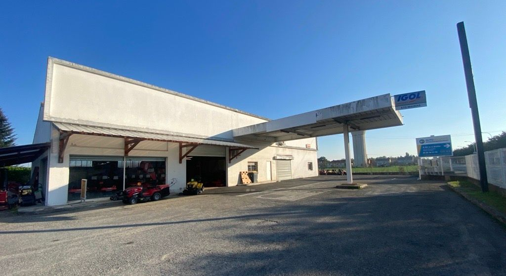 Tondeuse à gazon rouge sur l'herbe verte devant un hangar aux portes en bois ouvertes, baignée de soleil.