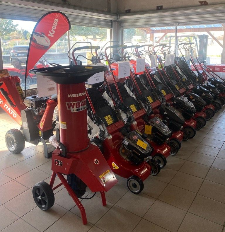 Présentoir d'équipements d'entretien de pelouse Stihl : tondeuses à gazon et coupe-bordures orange disposés dans un magasin.