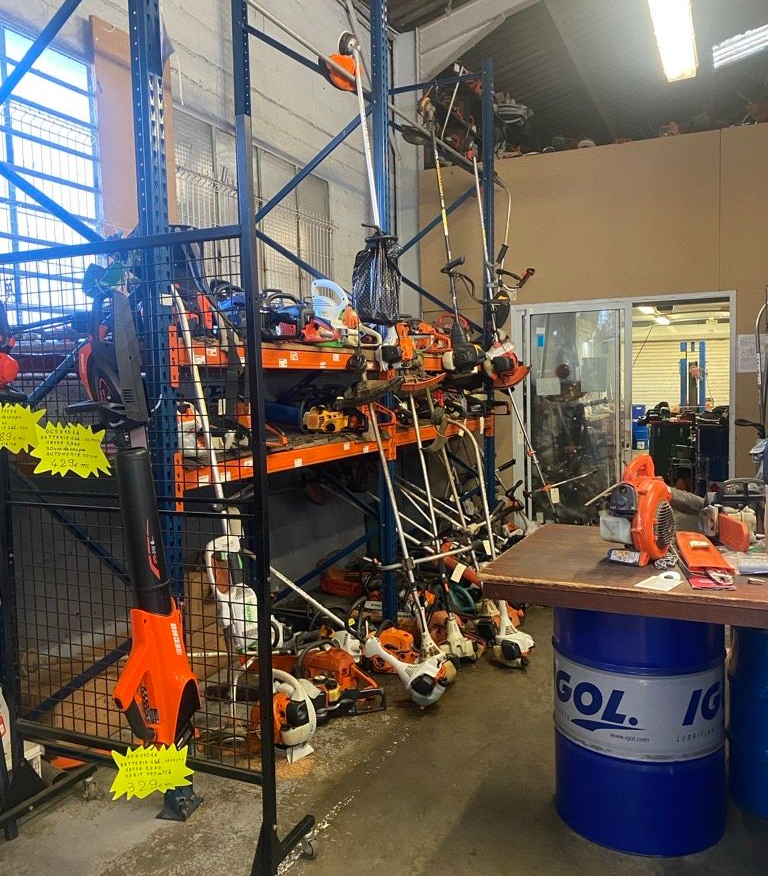Un homme portant des lunettes, une chemise à carreaux, au téléphone, prenant des notes à une table en bois près d'un mur.