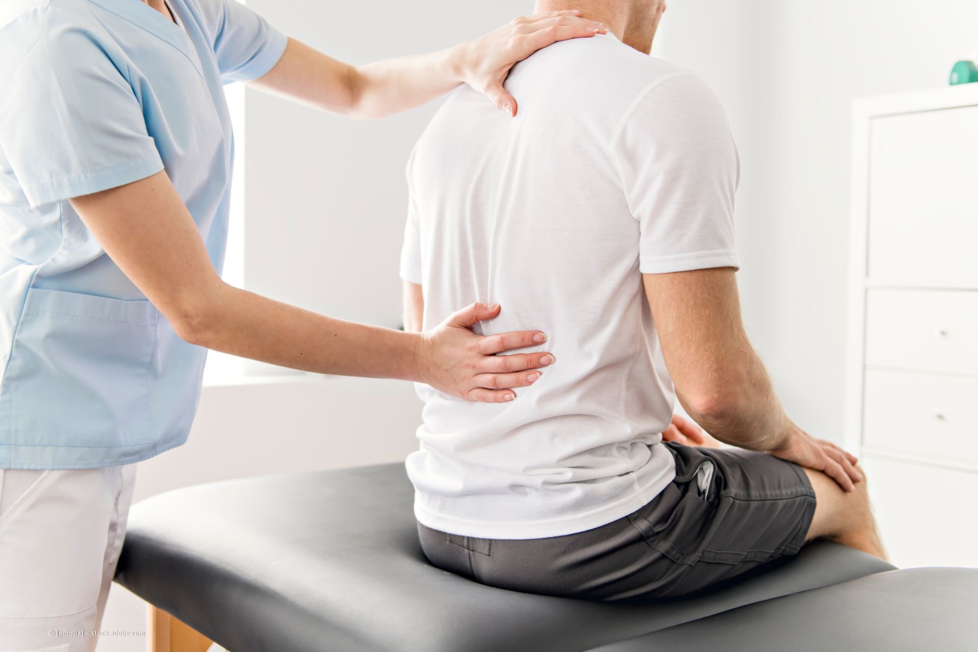 Ein Arzt untersucht den Rücken eines auf einer Behandlungsliege sitzenden Patienten.