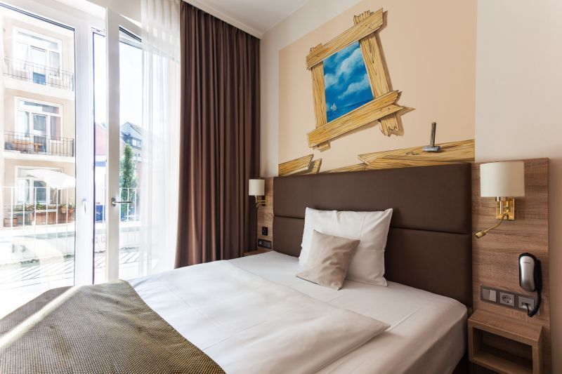 Hotelzimmer mit Bett, Fenster und einem bemalten Fenster an der Wand. Braun- und Beigetöne.