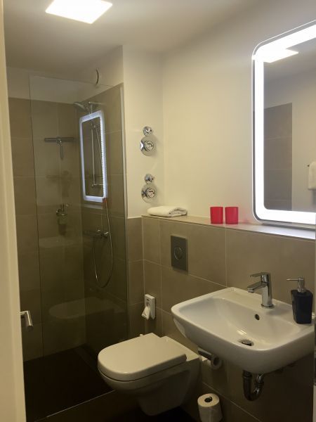 Modernes Badezimmer mit Dusche, Toilette, Waschbecken und Spiegel. Beige Fliesen und neutrales Farbschema.