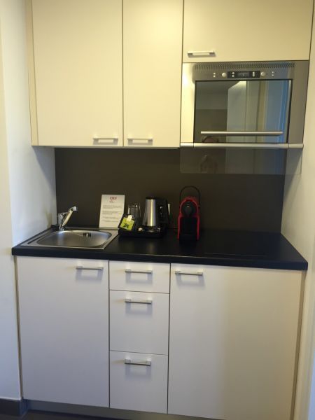 Kleine weiße Küche mit Spüle, Mikrowelle, Schränken und Kaffeemaschine.