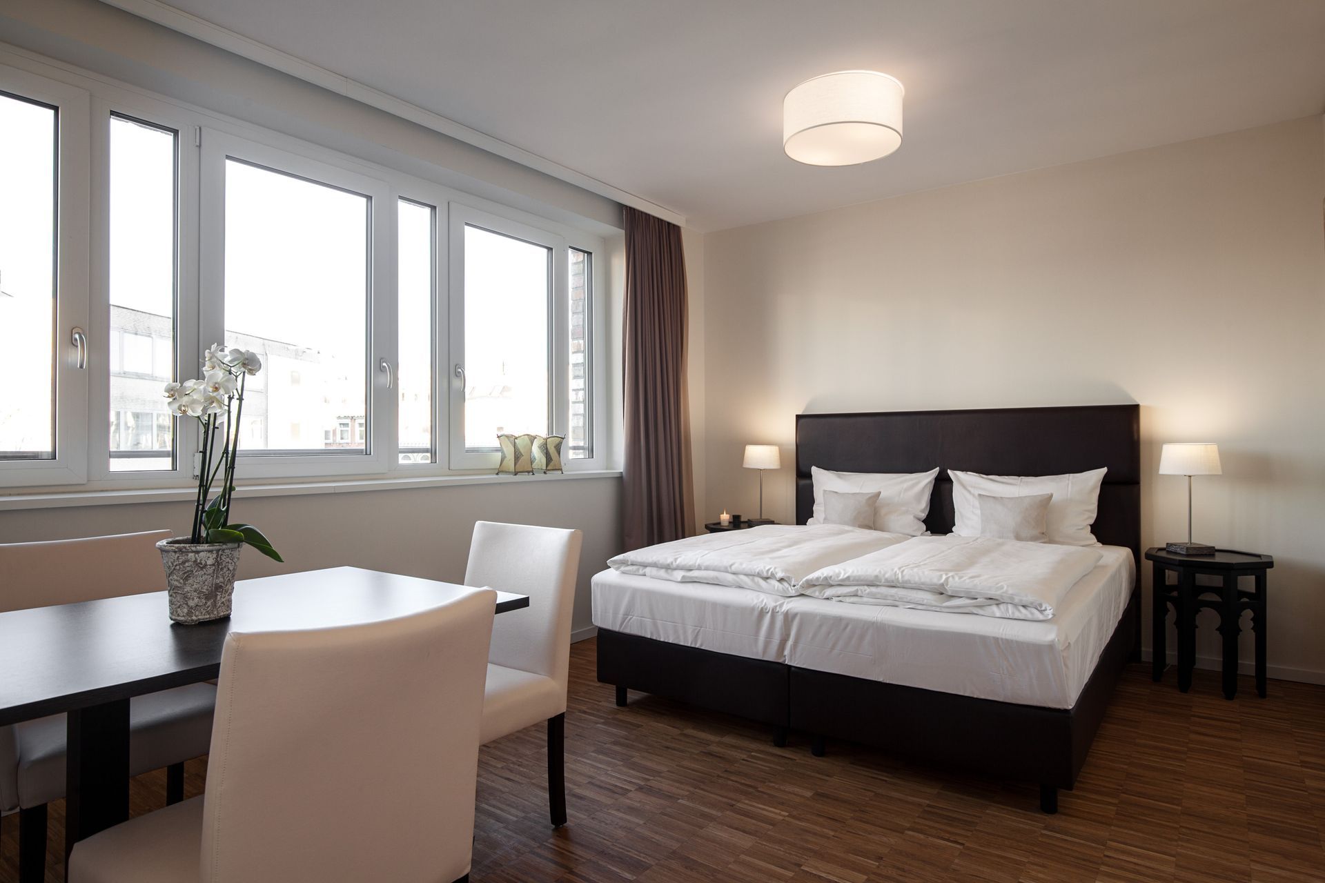 Schlafzimmer mit großem Bett, Esstisch und großen Fenstern.
