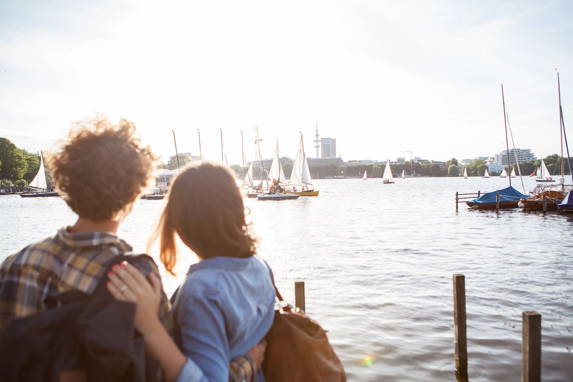 Ein Paar schaut sich Segelboote auf einem sonnigen See an und umarmt sich auf einem Holzsteg.