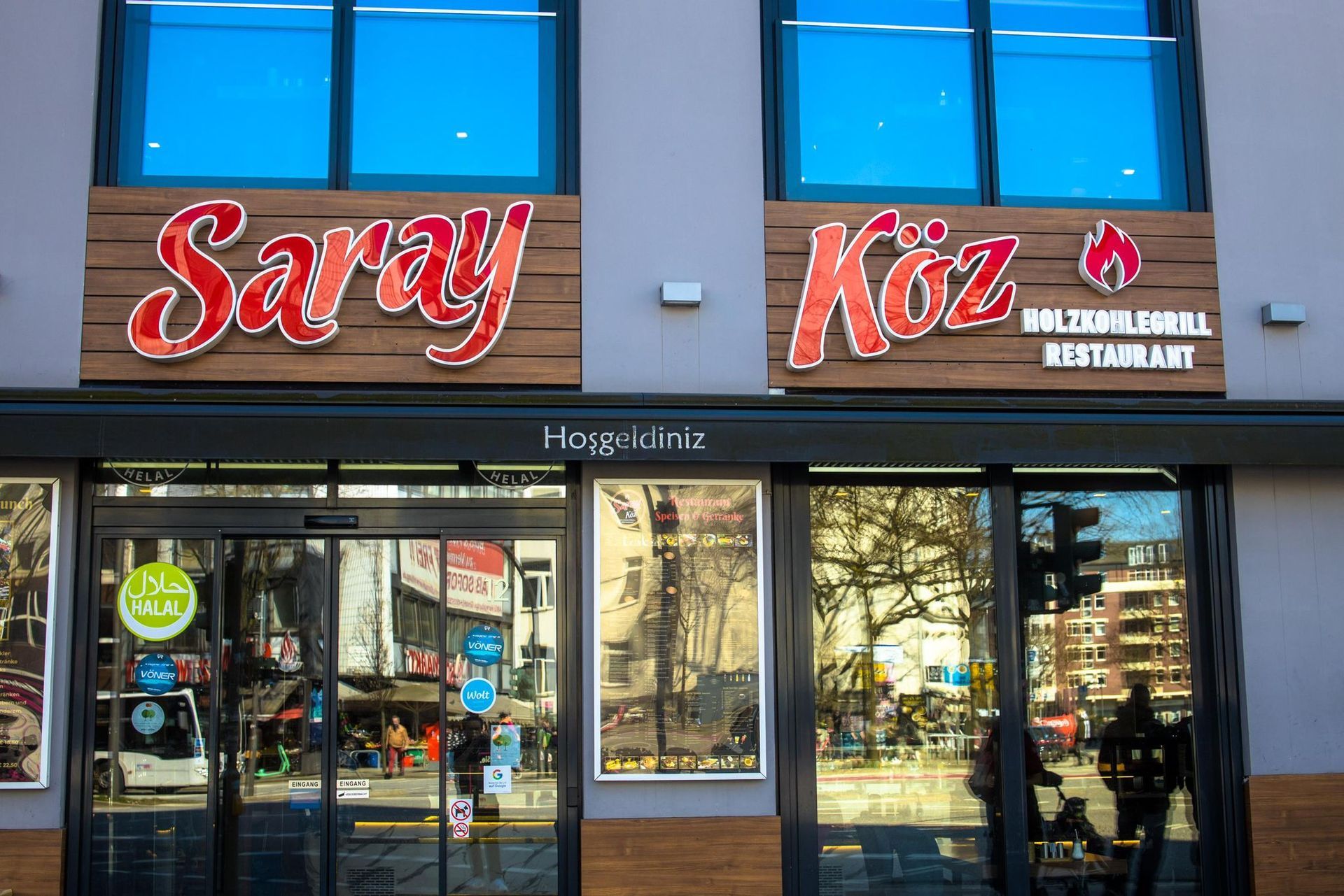 Restaurantfassade mit rotem „Saray Köz“-Schild, Fenster spiegeln Straßenszene wider.