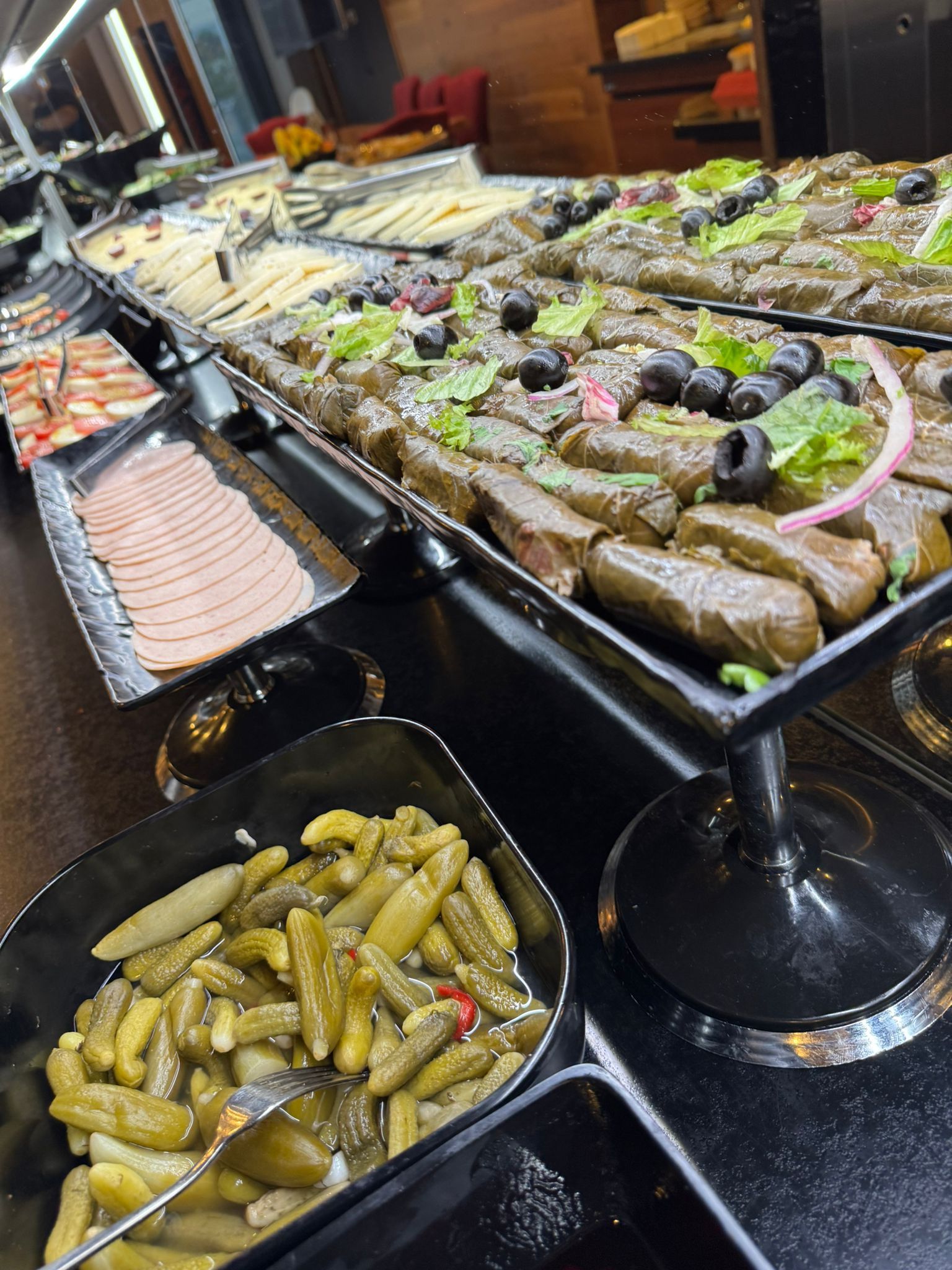 Ein Buffet mit Dolma, Pickles, Aufschnitt und anderen zubereiteten Speisen in schwarzen Servierschalen.