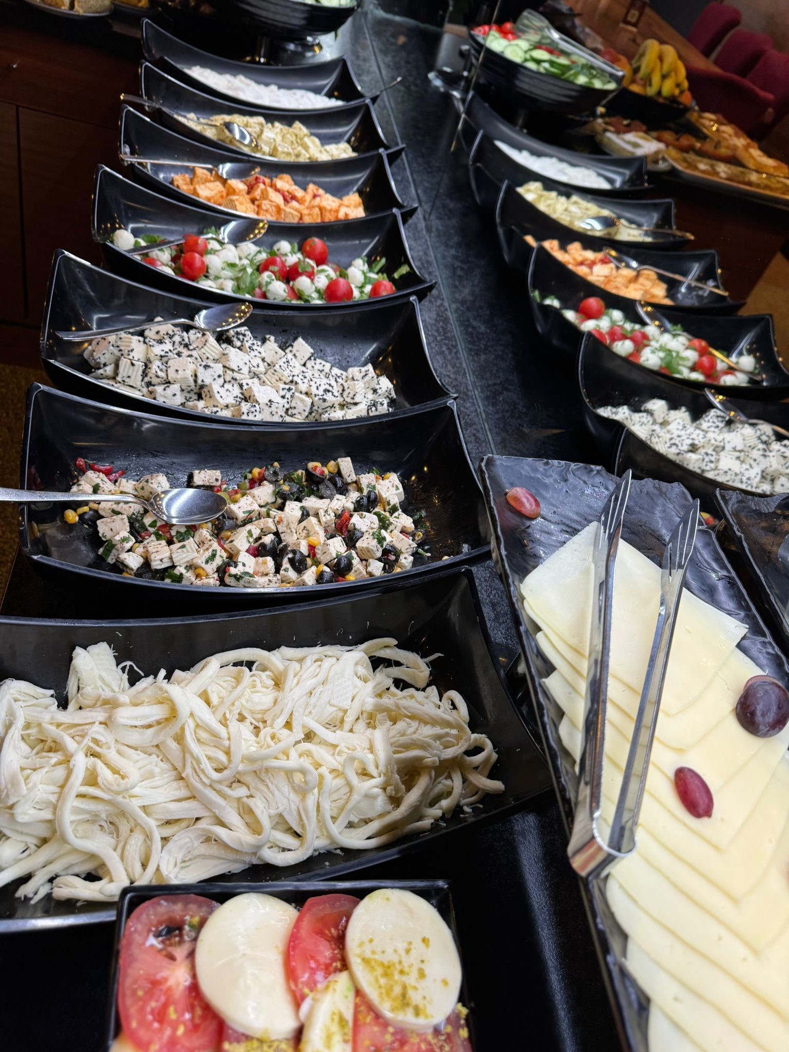 Buffet mit vielen Gerichten auf schwarzen Servierplatten, darunter Salate und Käse.
