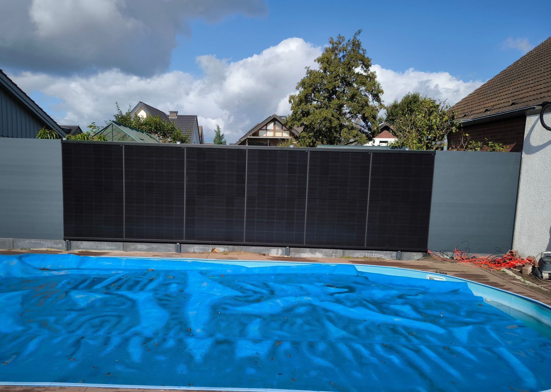 Ein Zaun umgibt einen Swimmingpool mit einer blauen Abdeckung darauf