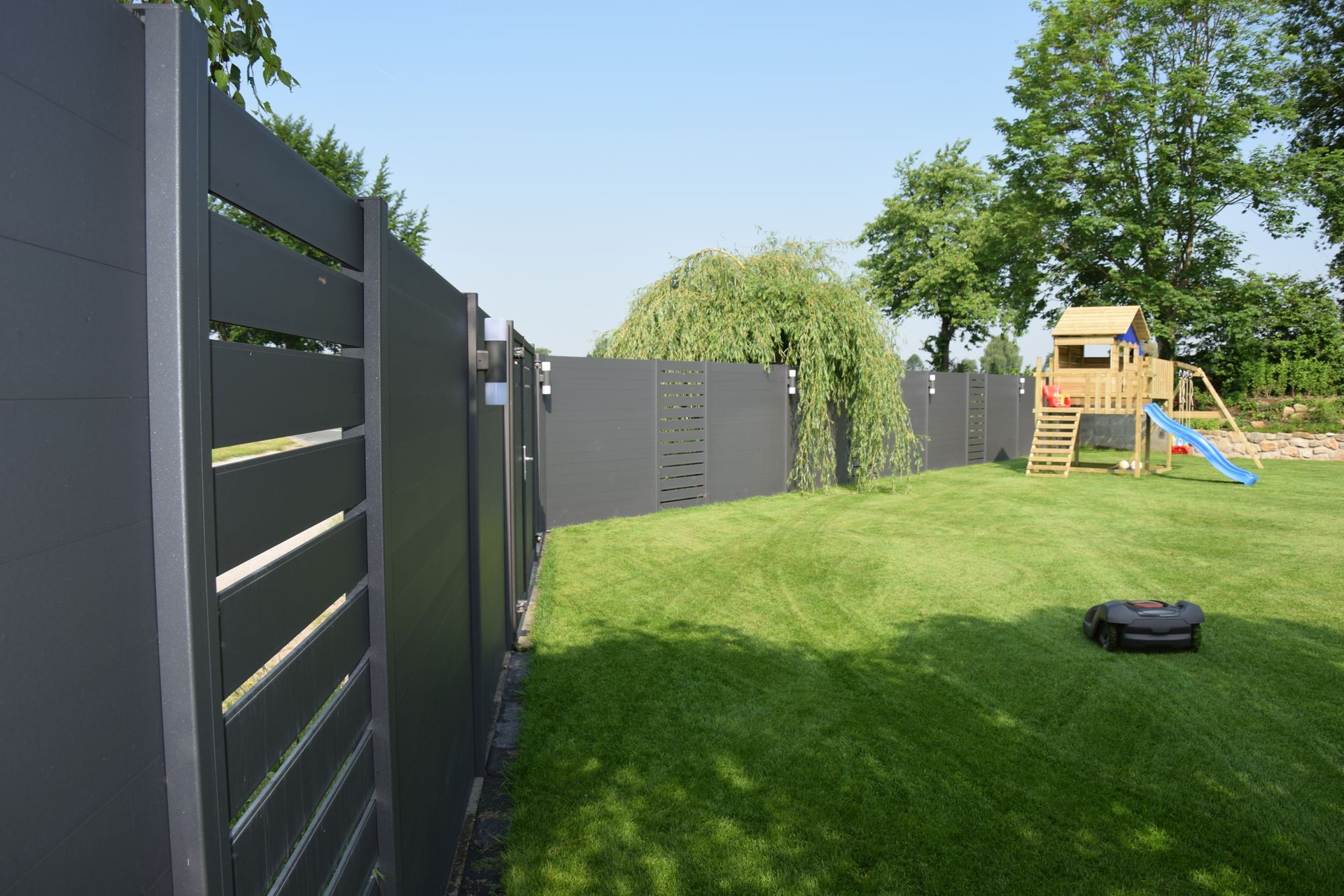 Ein Zaun umgibt einen üppig grünen Hof mit einem Spielplatz im Hintergrund.