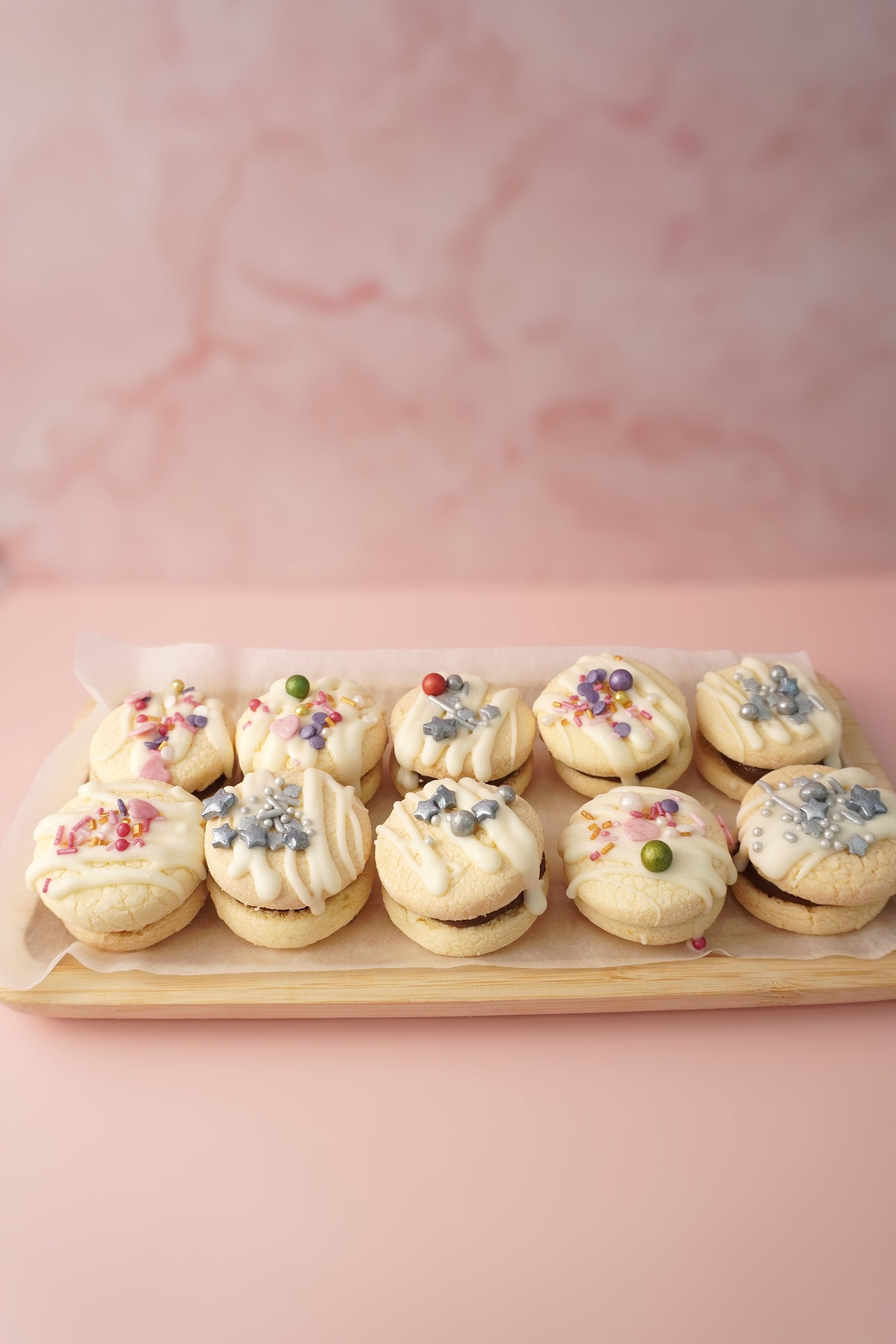 Galletas en una bandeja de madera, cubiertas con chispas, sobre un fondo rosa.