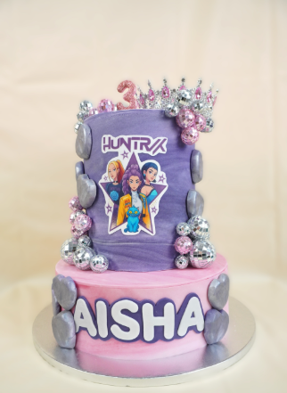 Pastel de dos pisos con una imagen de dibujos animados. Piso superior: morado. Piso inferior: rosa con la palabra