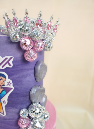 Pastel morado decorado con una corona, bolas de discoteca y una princesa de dibujos animados.