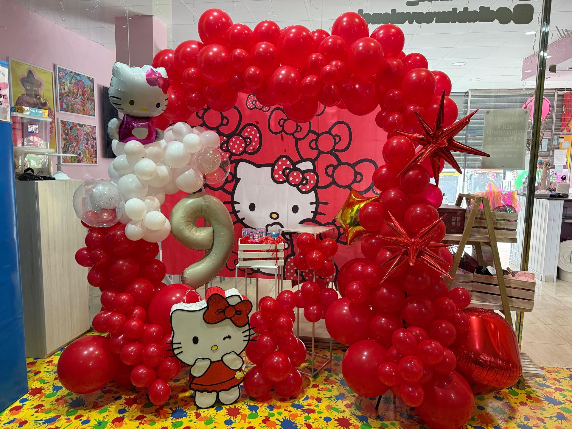 Decoración de fiesta de Hello Kitty con globos rojos, arco y fondo. Incluye un globo con el número