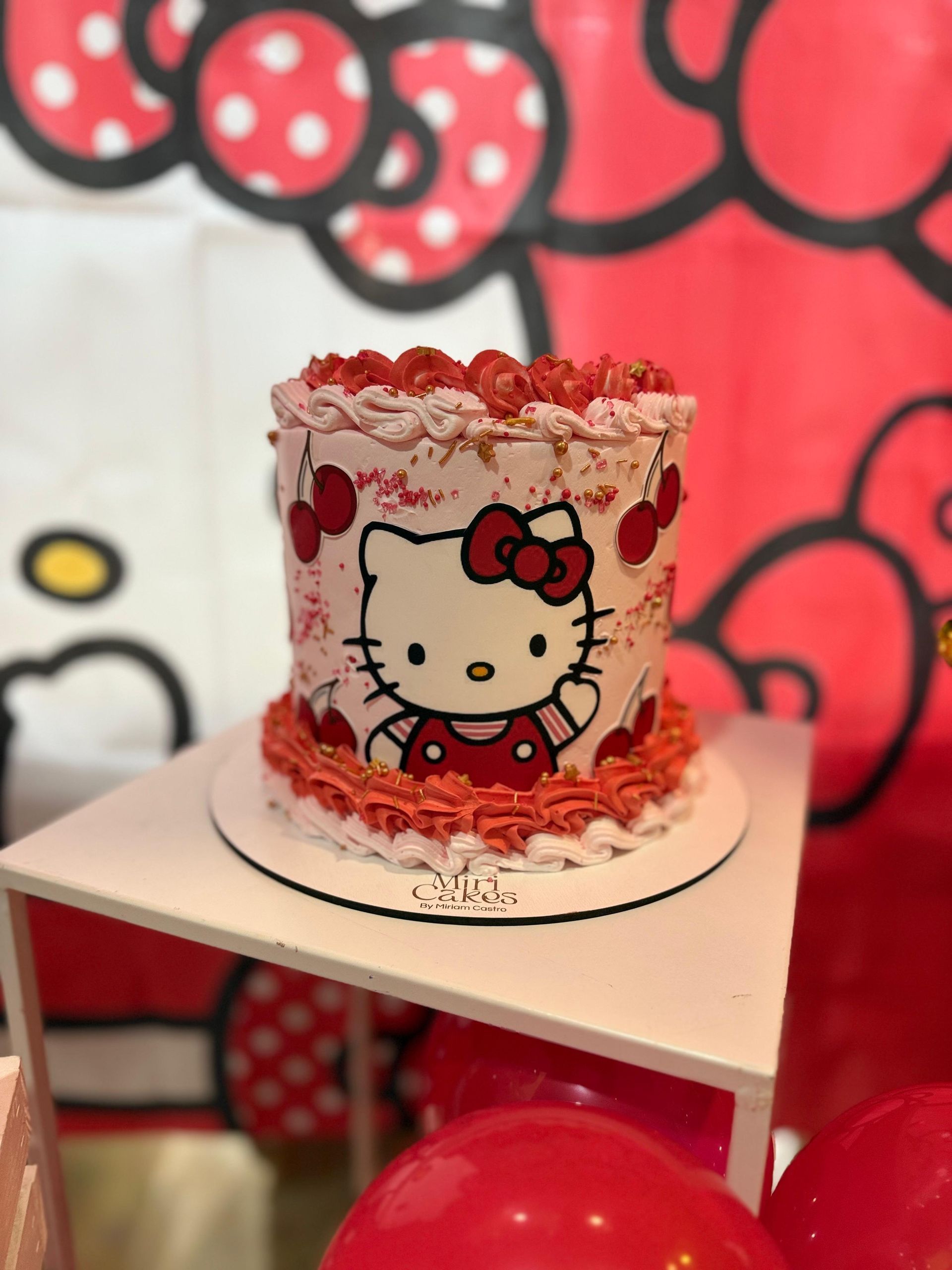 Pastel de Hello Kitty con glaseado rojo y blanco, decoraciones de cerezas.
