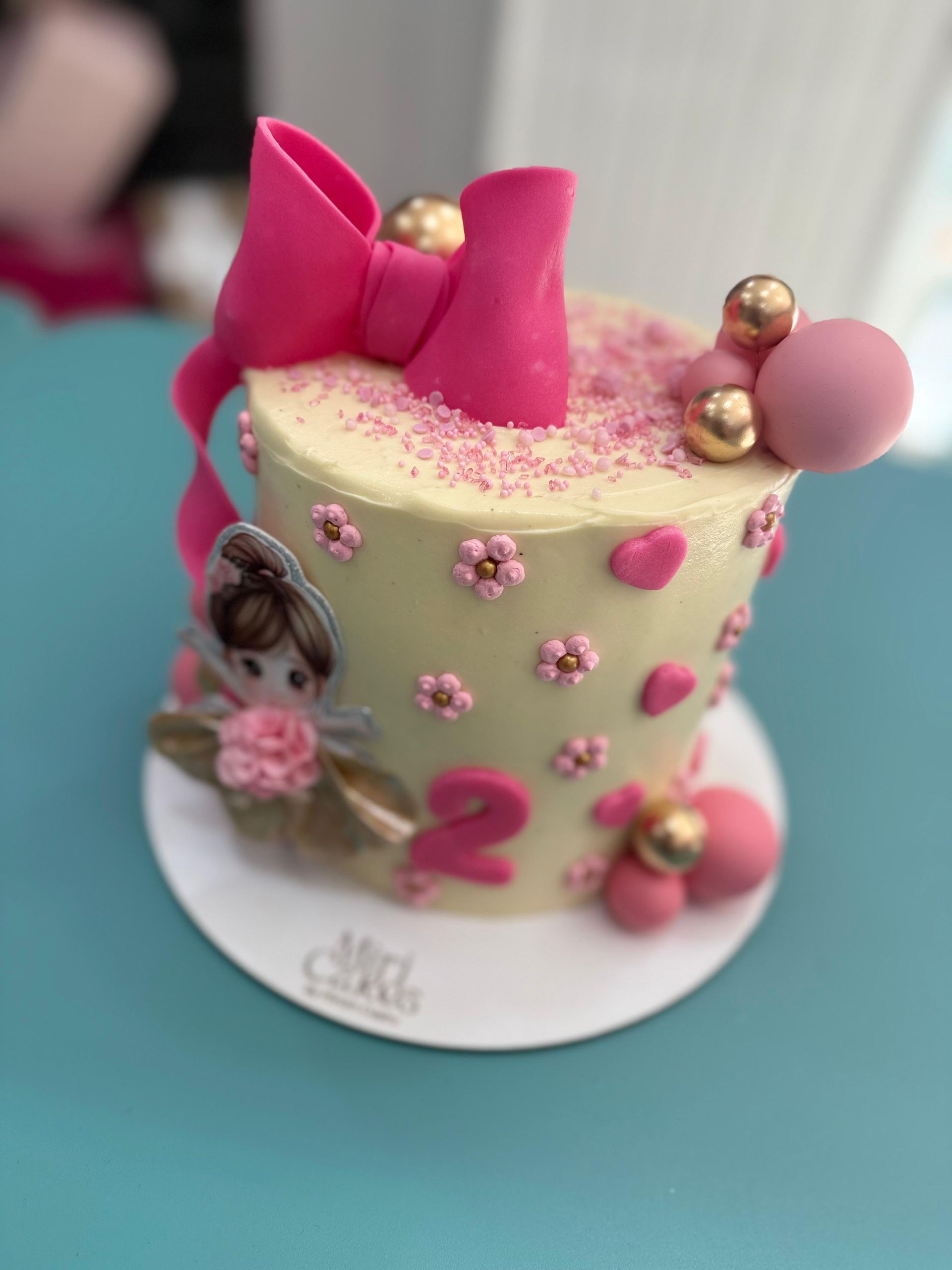 Pastel decorado en color rosa con un lazo, una bailarina y el número 2 sobre una base blanca.
