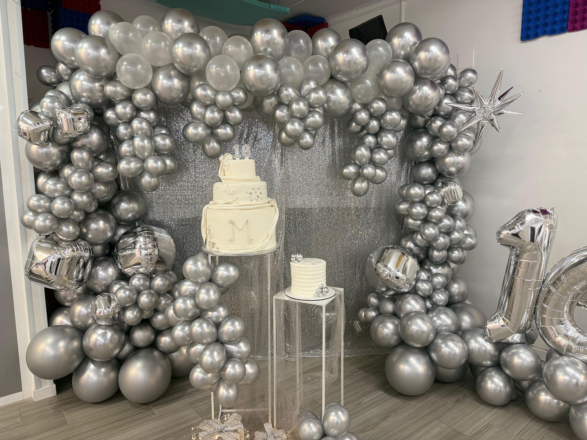 Arco de globos plateados con soporte para pastel y pastel decorado.