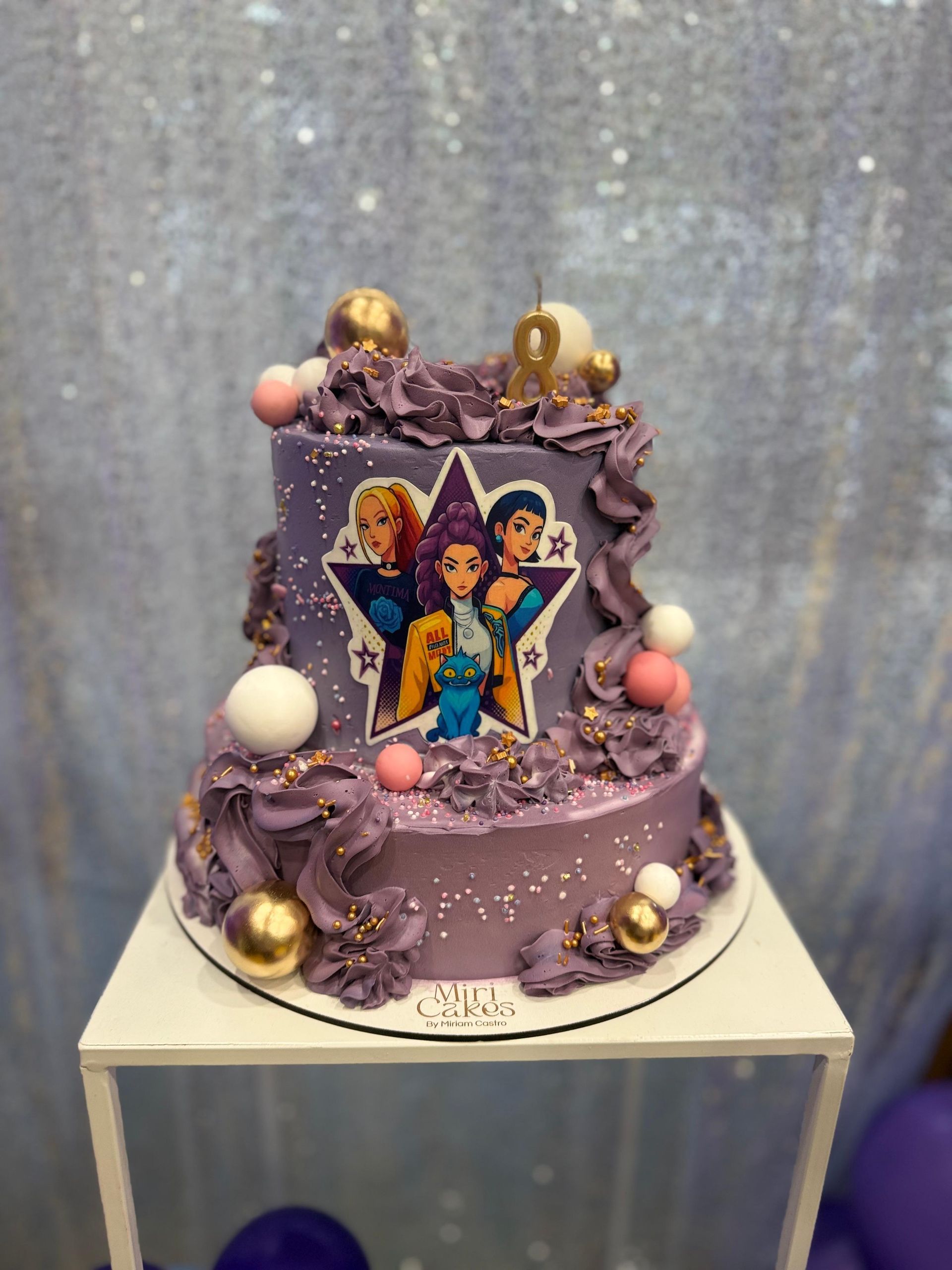 Pastel morado de dos niveles con personajes de dibujos animados, detalles dorados y una vela con el número 9 sobre una mesa blanca.