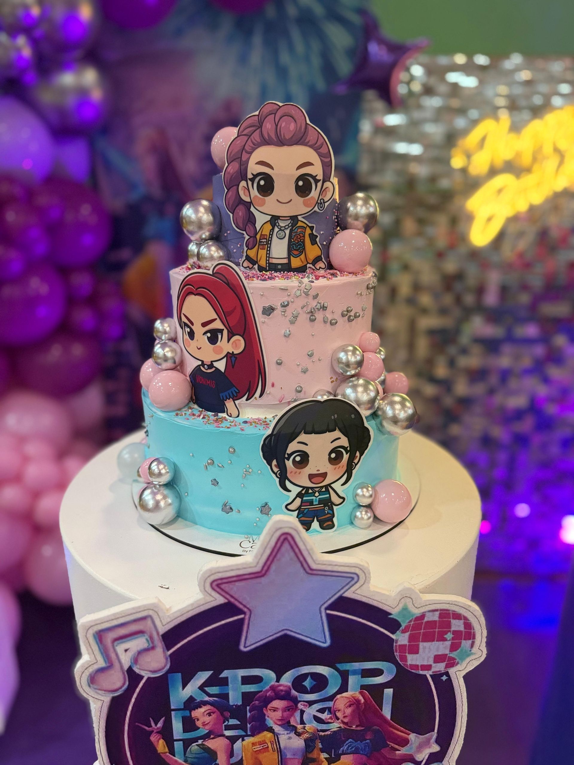 Pastel con temática de K-Pop con personajes de dibujos animados, glaseado rosa y azul, decoraciones plateadas y recorte de estrella.