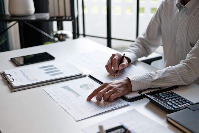 Une personne travaillant à un bureau, consultant des documents et utilisant une calculatrice.