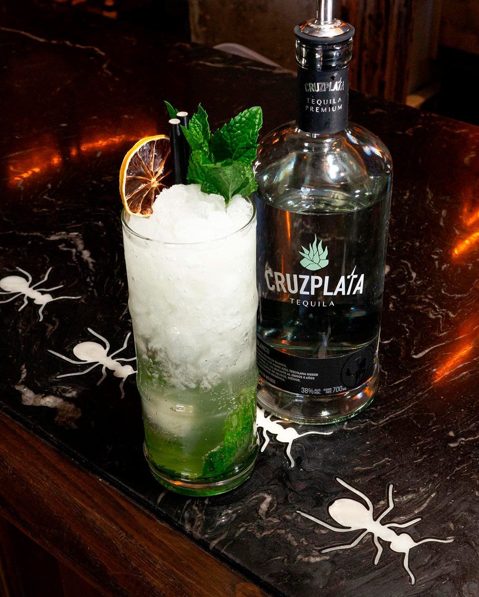 Una botella de tequila cruz plata junto a un vaso de bebida