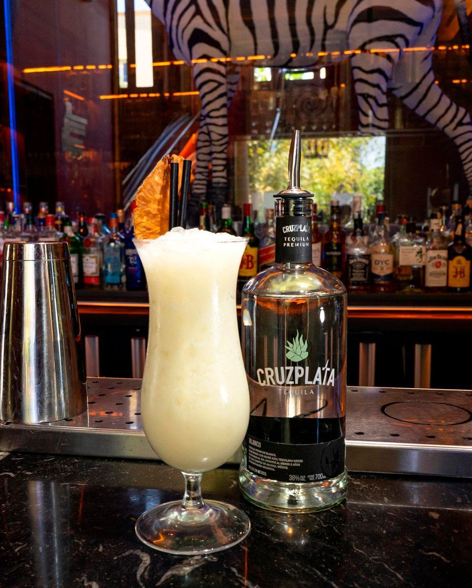 Una botella de cruz plata junto a un vaso de bebida