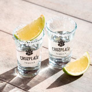 Dos vasos de tequila cruz plata con una rodaja de limón sobre una mesa de madera.
