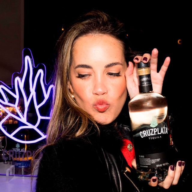 Una mujer sostiene una botella de tequila cruzplata en su mano.