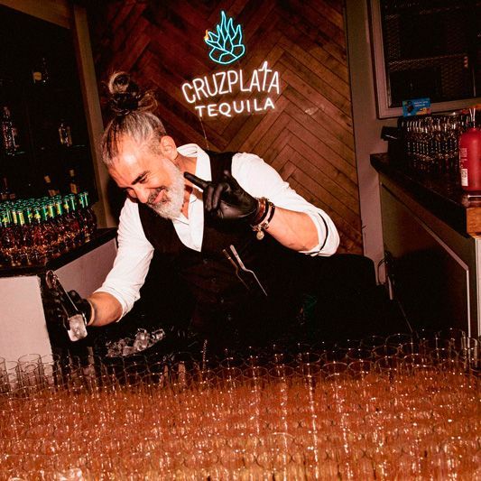 Un camarero está preparando una bebida delante de un cartel que dice tequila cruz plata.