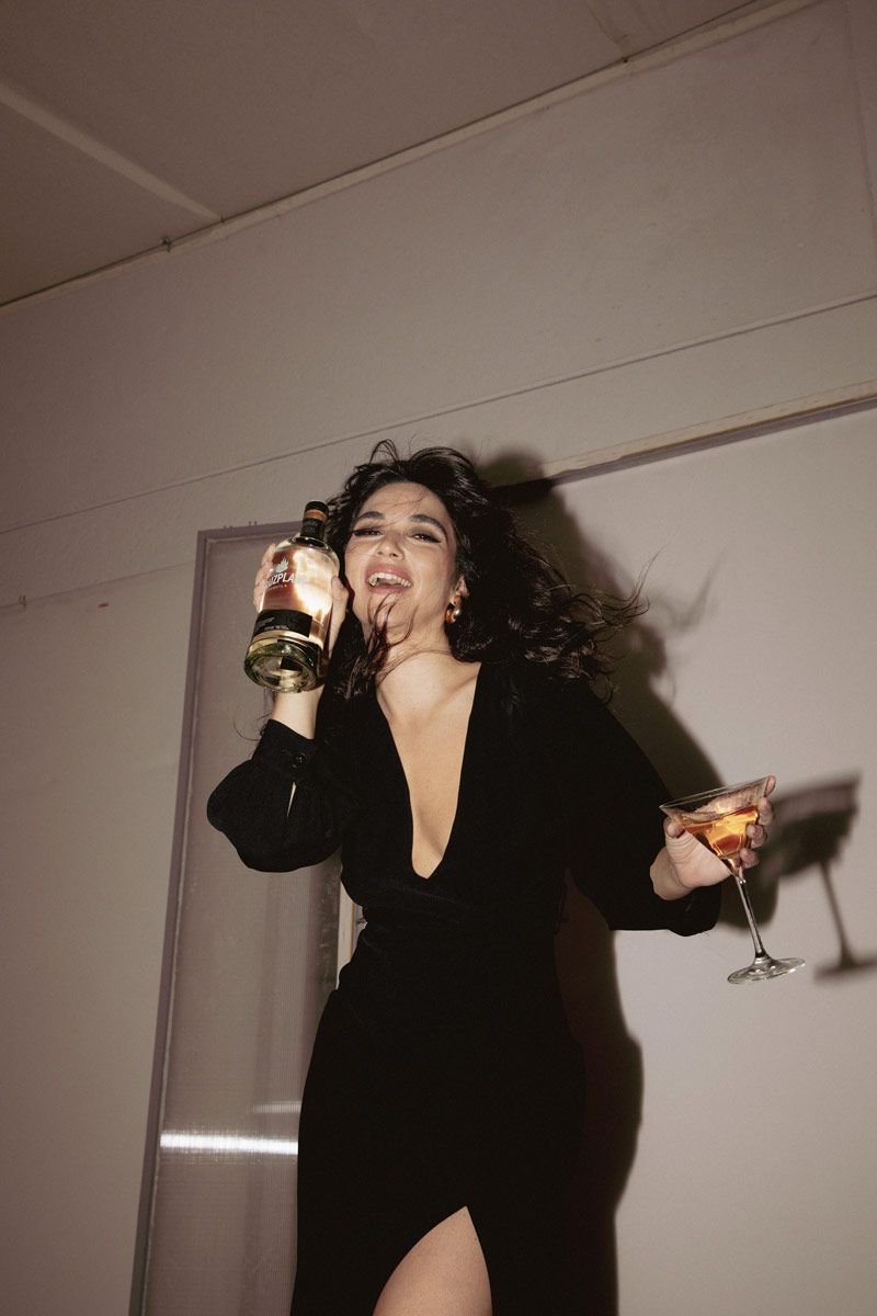 Una mujer vestida de negro sostiene una botella de vino y una copa de vino.